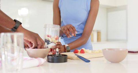 African american couple preparing fresh fruit smoothie at bright white kitchen island