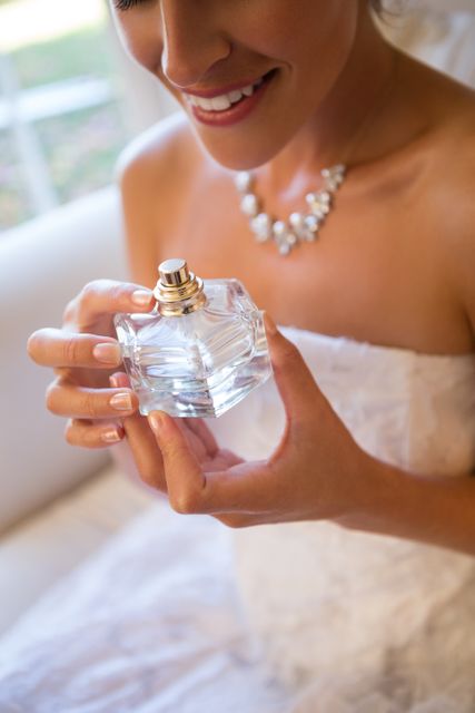 Midsection of smiling bride holding perfume sprayer while sitting on armchair at home