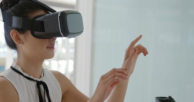 Woman wearing VR headset indoors, interacting with virtual environment by pointing her finger. Ideal for technology, VR experiences, interactive content, modern gadgets, futuristic concepts, and tech-focused advertisements.