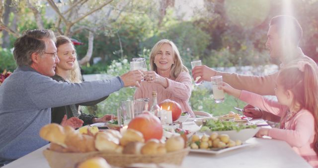 Family enjoying an outdoor meal while raising glasses for a toast. Ideal for depicting family bonding, celebrations, outdoor dining experiences, and creating a happy, warm atmosphere in advertisements, brochures, and social media promotions.