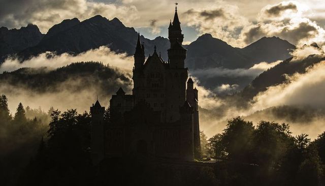 Misty alpine castle silhouette at sunrise with dramatic fog and mountain ridges - fairy fortress