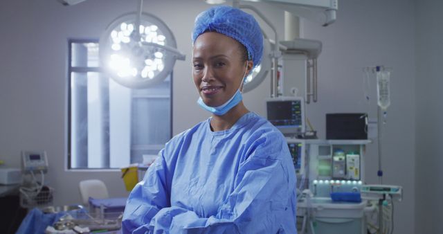 Portrait of biracial female surgeon wearing lowered face mask smiling in operating theatre. medicine, health and healthcare services during covid 19 coronavirus pandemic.