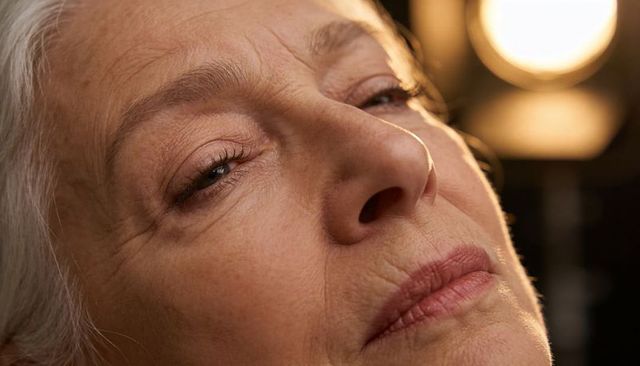 Tilting senior woman revealing detailed facial texture under warm circular studio light