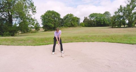Golfer practicing shot from sand bunker on sunny day