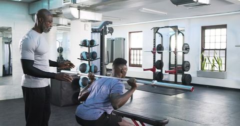 Fitness trainer assisting senior client with squat in modern gym