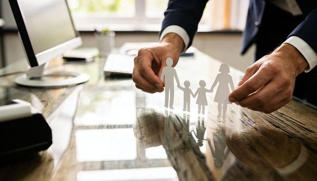 Businessperson placing paper family cutout on glossy wooden desk with reflections