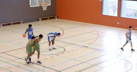 Basketball Players Competing on Indoor Court Under Hoop