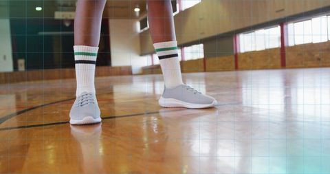 Athletic lower legs standing on polished hardwood basketball court wearing striped socks
