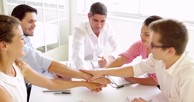 Business team showing unity and celebrating their success by placing hands together in an office meeting. This image can be used to represent teamwork, corporate achievements, and professional cooperation. Ideal for business presentations, teamwork motivational posters, corporate websites, and company promotional materials.
