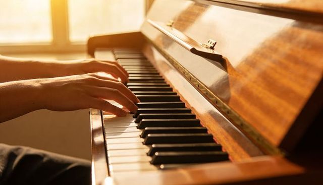 Sunlit hands playing piano on warm wood upright keys, close-up music practice and teaching