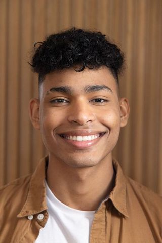 Smiling african american teen wearing brown shirt and white tee with wood slat backdrop