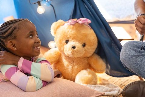 African american child playing in cozy blanket fort with parent and teddy bear under lights