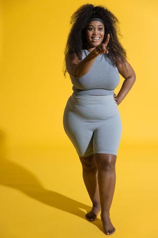 Confident african american woman pointing and smiling in gray activewear on yellow studio