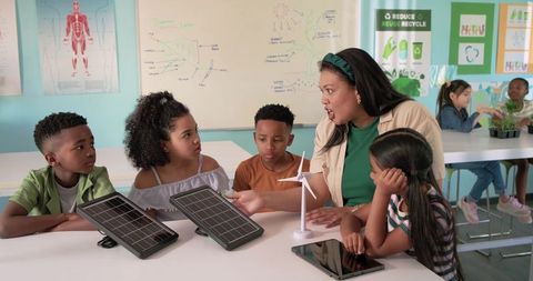Diverse teacher leading renewable energy lesson with solar panels wind turbine