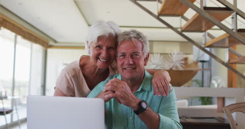 Happy Senior Couple Embracing at Home Using Laptop
