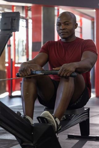 Mature man rowing on ergometer in gym wearing maroon shirt showing focused endurance