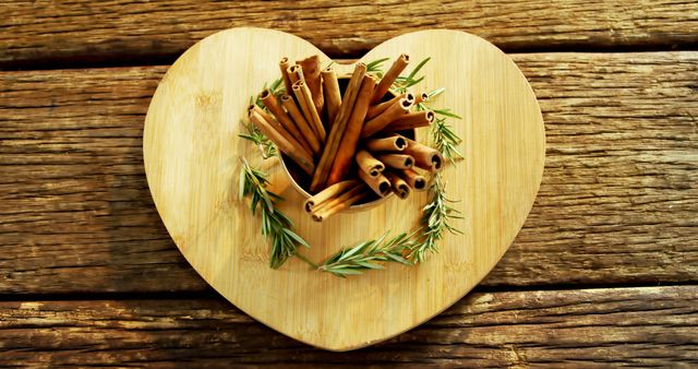 Cinnamon sticks and fresh rosemary sprigs are arranged on a heart-shaped wooden plate, symbolizing warmth and aromatic flavors. This composition suggests a cozy, homey vibe often associated with festive or culinary themes.