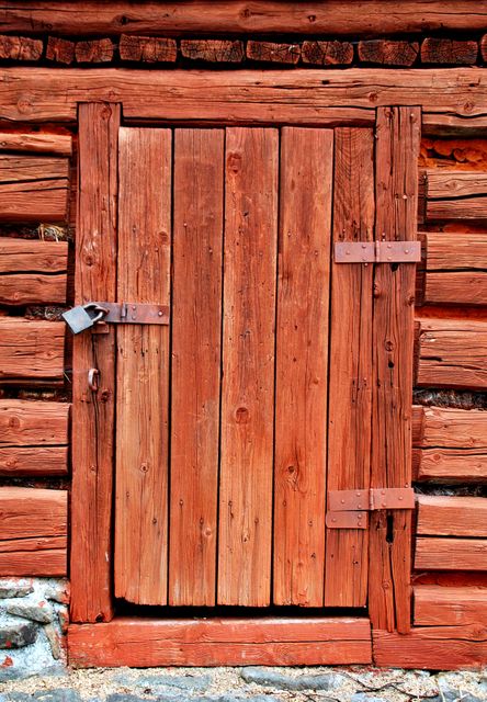 Old wooden door in a rustic log cabin featuring weathered wood and a padlock. Ideal for themes involving rural life, history, or traditional architecture. Can be used for illustrating articles about countryside living, vintage designs, or historical structures.
