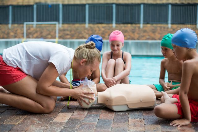 Lifeguard demonstrating CPR techniques to a group of children by the poolside. Ideal for use in educational materials, safety training programs, summer camp promotions, and health and wellness campaigns.