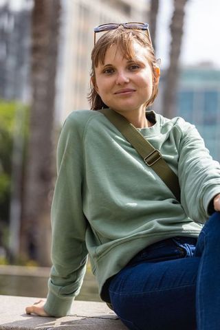 Young woman relaxing on urban plaza ledge wearing green sweatshirt and sunglasses