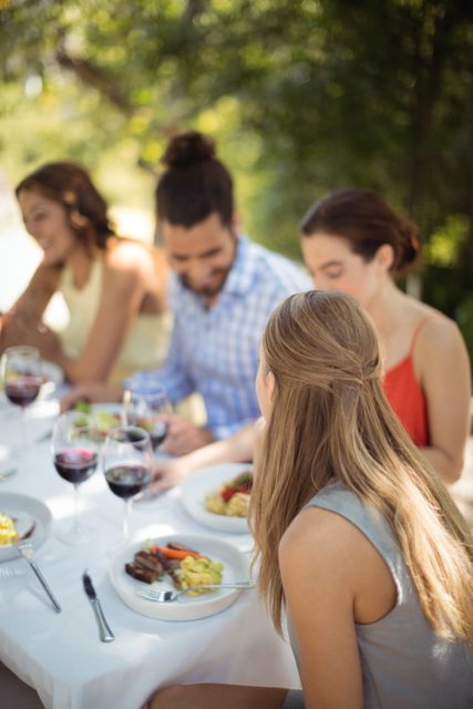 Group of friends enjoying lunch at an outdoor restaurant, engaging in conversation and sharing a meal. Ideal for use in advertisements for restaurants, social events, or lifestyle blogs focusing on dining and social gatherings.