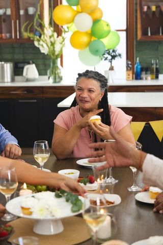 Mature woman enjoying cupcake during multigenerational kitchen celebration with balloons