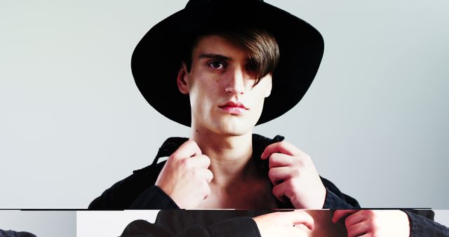 A young Caucasian man wearing a wide-brimmed hat looks directly at the camera, with copy space. His serious expression and stylish attire suggest a fashion-forward individual or a model posing for a portrait.