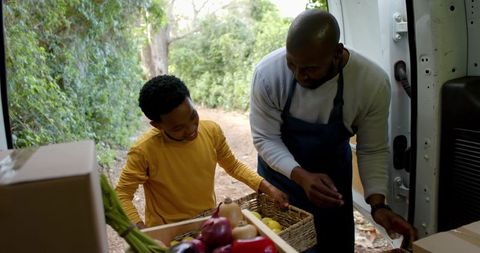 African american father and son arranging fresh produce at mobile market van outdoors