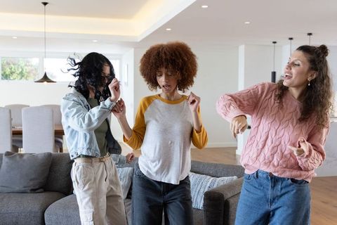 Diverse friends dancing in modern open-plan living room enjoying casual home gathering