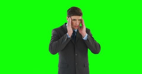 Stressed businessman with headache against green screen
