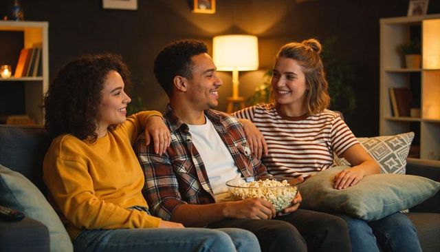 Friends watching movie together on cozy living room sofa with popcorn bowl evening hangout