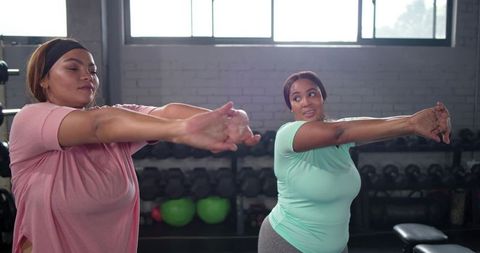Plus-size women stretching together in gym doing chest stretch for body positive fitness