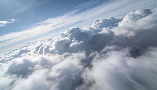 Sunlit cumulonimbus towers rising over expansive cloudscape, high-altitude aerial view