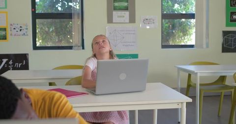 Teen girl looking up in classroom with silver laptop and classmates daydreaming