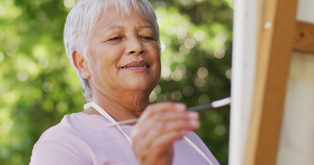 Image of happy biracial senior woman painting in garden. active retirement lifestyle, hobby and spending time outdoors.