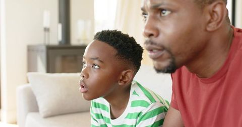 African-american father and son watching tv together on couch showing focused bond