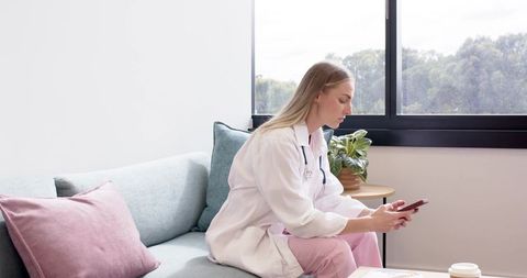 Female clinician checking smartphone while sitting on clinic sofa in natural light