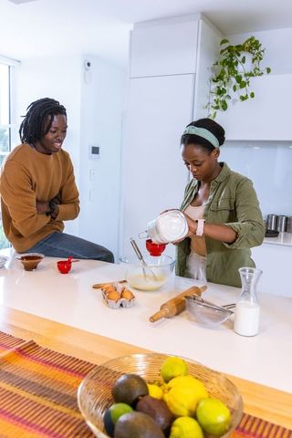 African american couple baking together on bright kitchen island pouring flour into mixing bowl