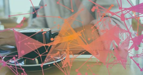 Typing on laptop beside coffee cup with pink-orange digital network overlay