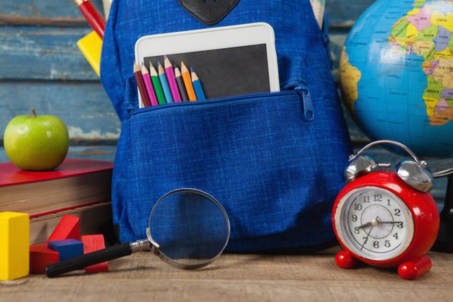 Close-up of school supplies, apple, globe, digital tablet and magnifying glass on wooden table