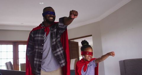 Joyful father and daughter in superhero costumes at home