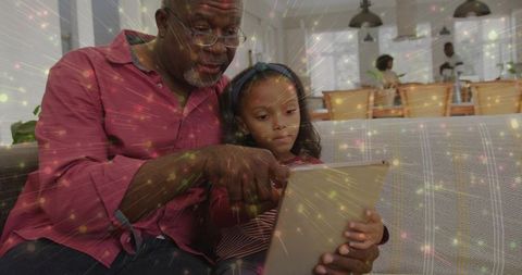 Grandfather and Granddaughter Sharing Tablet, Exploring Digital World Together on Couch