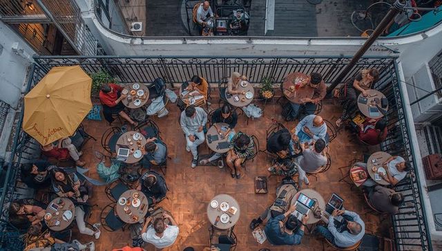 Rooftop cafe coworkers working and socializing while eating pastries under yellow umbrella