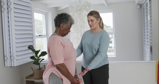 Senior woman working out at home with guidance from personal trainer. Trainer providing support and instructions. Scene emphasizes wellness, healthy lifestyle, and fitness for elderly. Ideal for use in articles or advertisements related to senior fitness, health and well-being programs, personal training sessions, and home exercise routines.