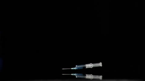 Syringe Dropping Against Black Background in Slow Motion