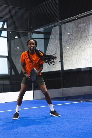 African American Athlete Serving on Paddle Court in Orange Shirt
