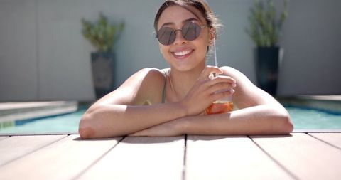 Smiling Woman in Sunglasses Relaxing Poolside with Drink
