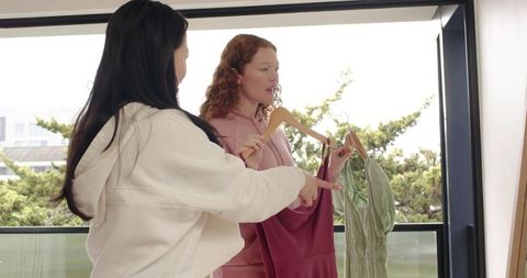 Women comparing dresses on sunlit balcony, choosing casual summer outfits and styling tips