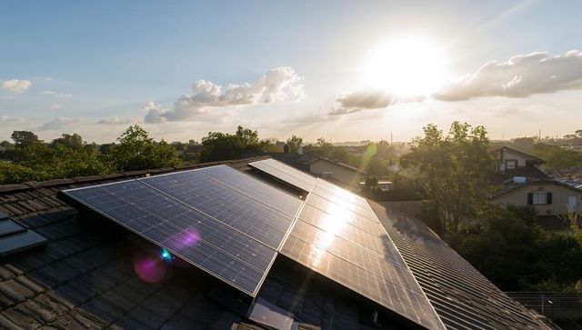 Sunlit solar panel array on sloped suburban rooftop reflecting morning sunlight