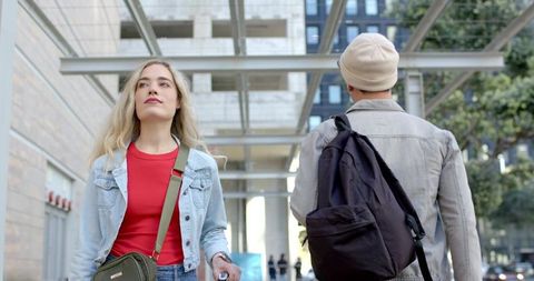 Young woman walking with rolling suitcase through modern glass and steel urban plaza